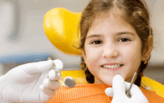 a little girl sitting in a chair with a dentist's hand holding tools at her mouth, representing early dental visits
