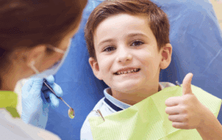 a child sitting in a chair with a dentist holding his thumb up, representing pediatric dentistry for special needs