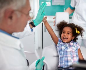 cheerful young girl in dental chair making joke with male dentist