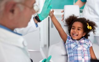 cheerful young girl in dental chair making joke with male dentist, child not scared of dentist